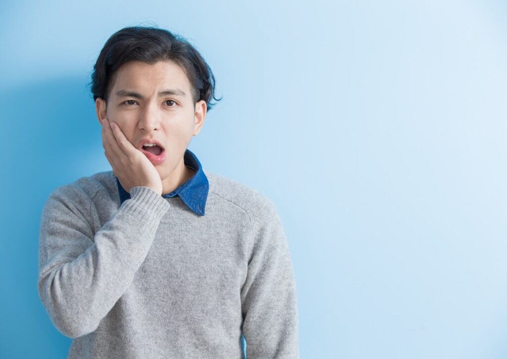 Person holding their jaw due to tooth pain, illustrating common symptoms that may require toothache relief treatment